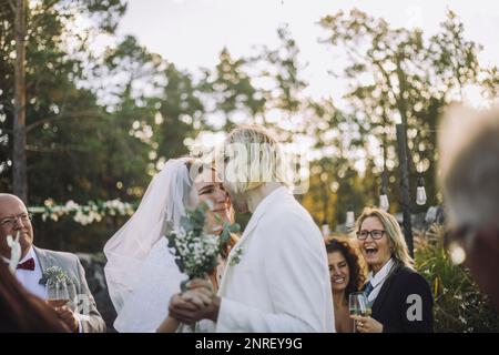 Happy bride and groom dancing together amidst guests during wedding ceremony Stock Photo