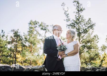 Smiling senior couple looking at each other while holding bouquet at wedding Stock Photo