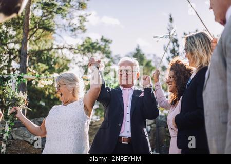 Happy married couple holding hands while dancing with family at wedding ceremony Stock Photo