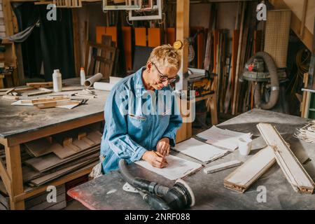 Female senior entrepreneur preparing document over workbench at repair shop Stock Photo