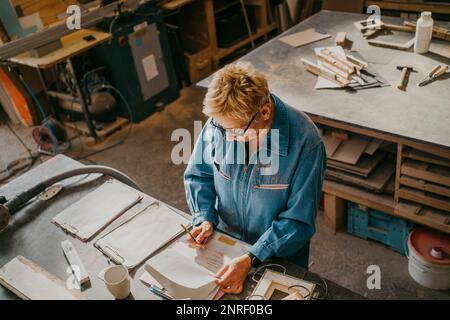 High angle view of senior craftswoman writing on document at workshop Stock Photo