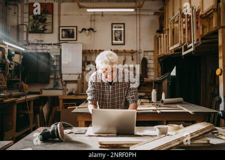 Senior male carpenter working on laptop at repair shop Stock Photo