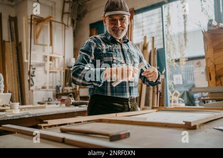 Focused senior male carpenter holding measuring tape at workshop Stock Photo