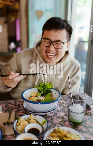 Happy young man having food with chopsticks at restaurant Stock Photo