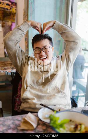 Happy young man making heart shape with hands while sitting at restaurant Stock Photo
