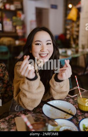 Portrait of smiling woman making heart shape with fingers at restaurant Stock Photo