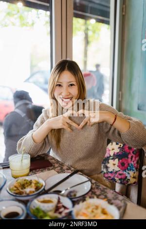 Portrait of happy woman making heart shape gesture while sitting at restaurant Stock Photo