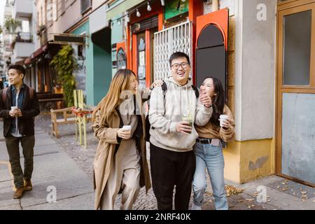 Cheerful male and female friends talking while walking on sidewalk Stock Photo