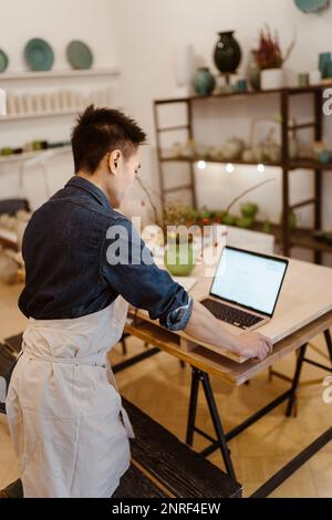 Male potter working on laptop while standing at workshop Stock Photo