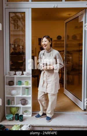 Young female potter laughing while standing at workshop doorway Stock Photo