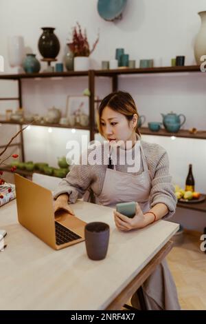 Potter using laptop on table while sitting at workshop Stock Photo
