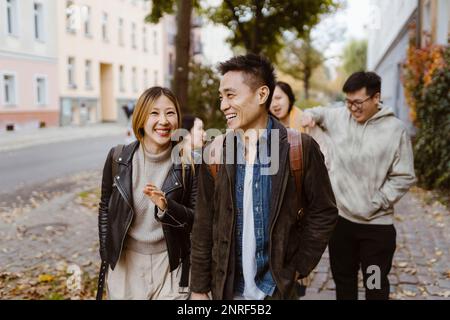 Male and female friends laughing while walking on sidewalk Stock Photo