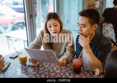 Male and female friends discussing while looking at menu card in restaurant Stock Photo