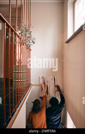 Rear view of couple taking measurement while hanging painting on wall at home Stock Photo