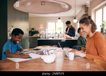Happy mother using laptop with son coloring in book while sitting at dining table in home Stock Photo