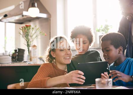 Smiling mother watching digital tablet with sons at home Stock Photo