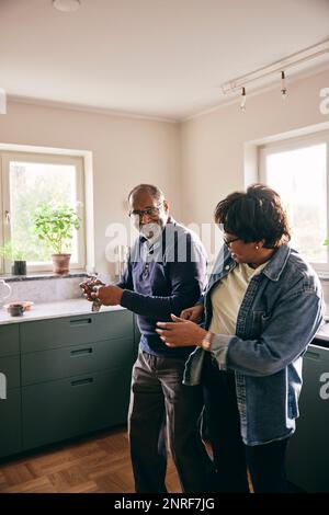 Playful senior couple dancing with each other while standing in kitchen at home Stock Photo