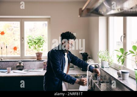 Side view of mature man filling pitcher from faucet in kitchen at home Stock Photo