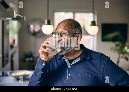 Contemplative senior man drinking water at home Stock Photo