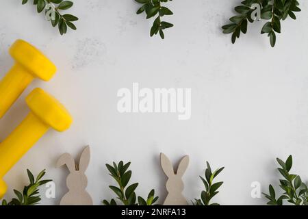 Dumbbells, boxwood branches, Easter bunny decorations. Healthy fitness composition, gym workout and training concept. Flat lay with copy space. Stock Photo