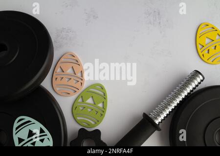 Dumbbells barbell weight plates and Easter wooden eggs decorations. Healthy fitness composition, gym workout and training flat lay with copy space. Stock Photo