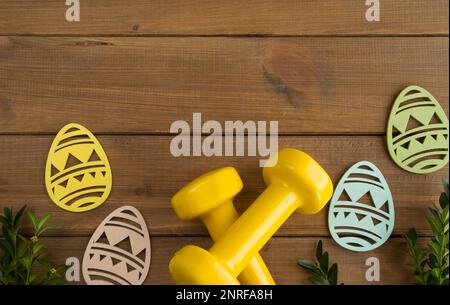 Dumbbells, boxwood branches, Easter wooden decorations. Healthy fitness composition, gym workout and training concept. Flat lay with copy space. Stock Photo