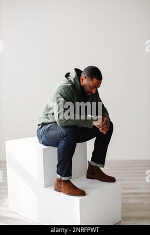 Fashionable Black man sitting and praying indoor Stock Photo