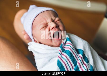 Yawning newborn baby wrapped in hospital blanket Stock Photo