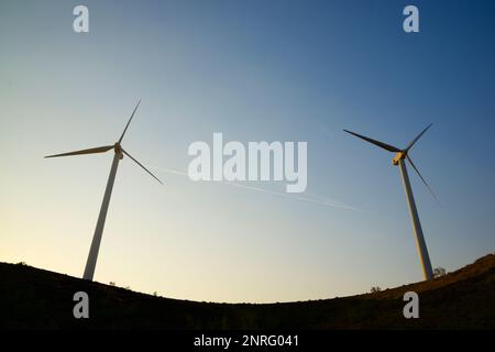Silhouettes of wind turbines on a hill at sunrise. Stock Photo