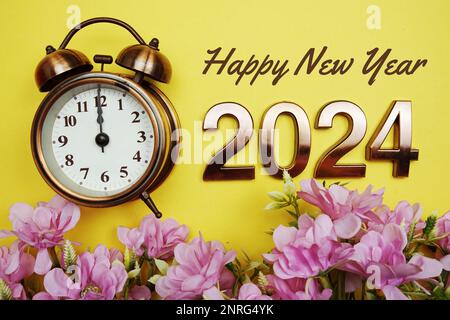 Happy New Year 2024 text with alarmclock and flower decoration on yellow background Stock Photo