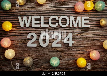 Welcome 2024 alphabet letters decorate with LED cotton balls on wooden background Stock Photo