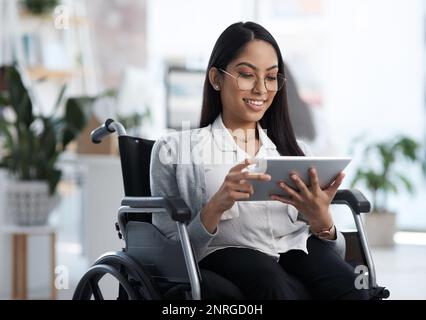 Working hard to achieve her goals. an attractive young businesswoman in a wheelchair using her tablet in the office. Stock Photo