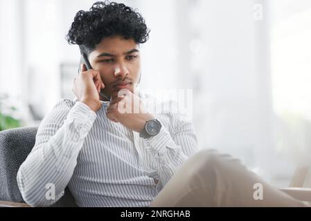 Lets brainstorm this some more. a young businessman looking thoughtful while talking on a cellphone in an office. Stock Photo