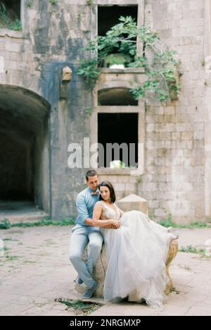 Bride and groom are sitting on a stone in the courtyard of the old fortress Stock Photo