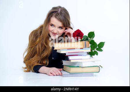 Studio shot of smiling schoolgirl doing her homework isolated over white background beautiful smart woman professor lies near books stack of large vintage books tome development focus banner  Stock Photo