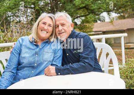 Portrait of happy elderly woman and man sitting at table in garden of nursing home Stock Photo