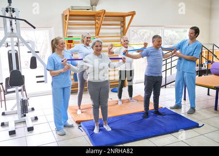 Male and female instructors assisting senior people doing workout with resistance bands at rehab center Stock Photo