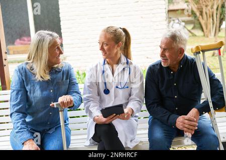 Female doctor explaining elderly woman and man over tablet PC in garden of nursing home Stock Photo