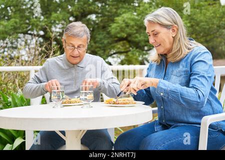 Smiling elderly woman and man having meal while sitting at table in garden of nursing home Stock Photo