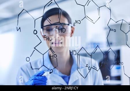 Each line of code connects. an attractive young female scientist working on a glass wipe board in her lab. Stock Photo