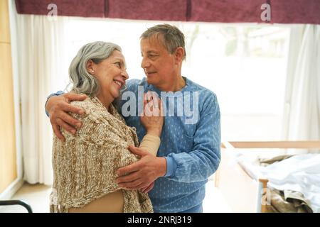 Senior man embracing and looking at smiling woman while standing in nursing home Stock Photo