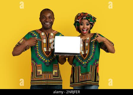 Bright black couple in african costumes holding laptop, mockup Stock Photo