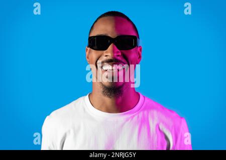 Cheerful young black man wearing sunglasses posing in neon light Stock Photo