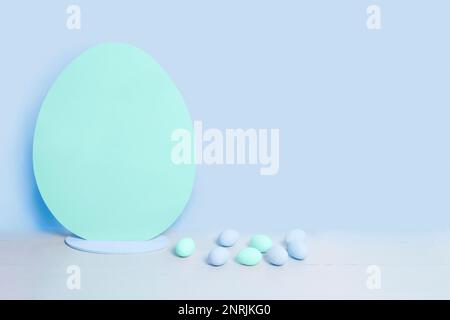 Big blank turquoise Easter egg and small blue and turquoise easter eggs on the background of blank blue wall. Minimalist Easter background Stock Photo
