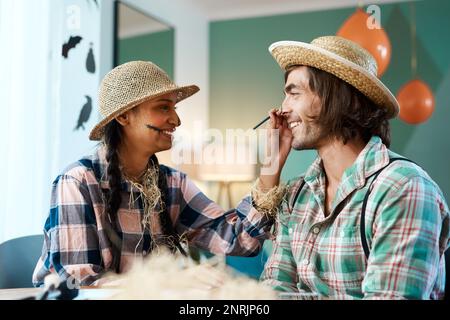 Makeup just makes it so much better. a young woman applying makeup to a young man at home. Stock Photo