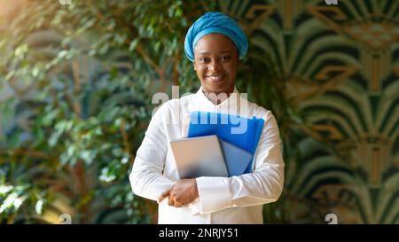 Pretty black lady posing at cafe, holding pad, notebook Stock Photo