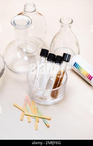 test tubes with liquids and solutions, flasks and indicator papers on light desk Stock Photo