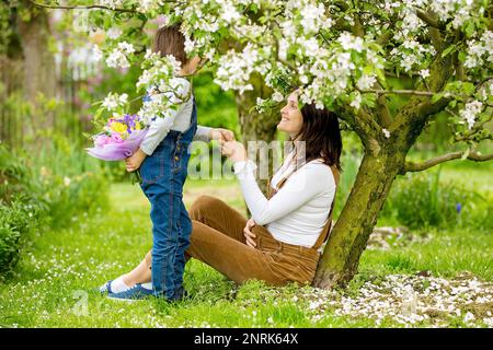 Young pregnant woman, receiving bouquet of colorful flowers from her child for Mothers Day, sitting in a beautiful spring blooming garden Stock Photo