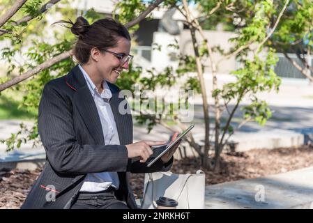 Female entrepreneur with glasses using digital tablet while sitting outdoors. Stock Photo