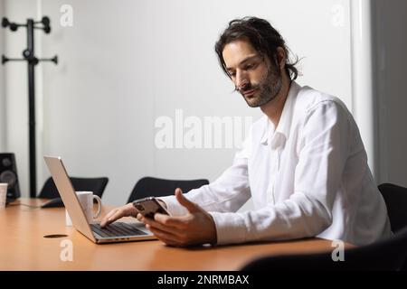 portrait of a man working on his laptop and using his phone to communicate. He is sitting in a nice office Stock Photo